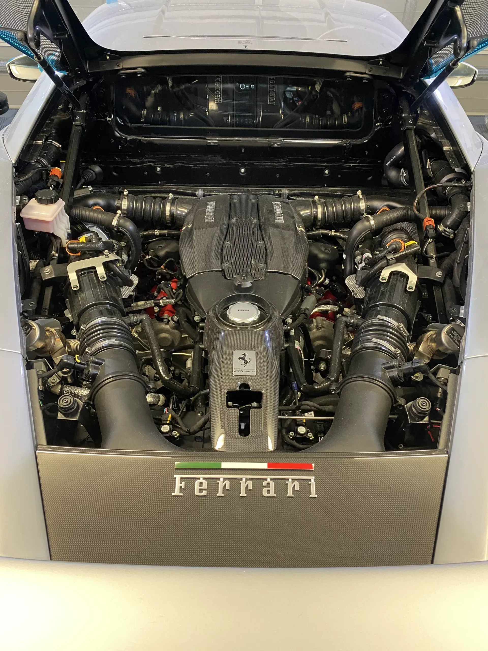Ferrari engine bay with carbon fiber components, Italian flag emblem.
