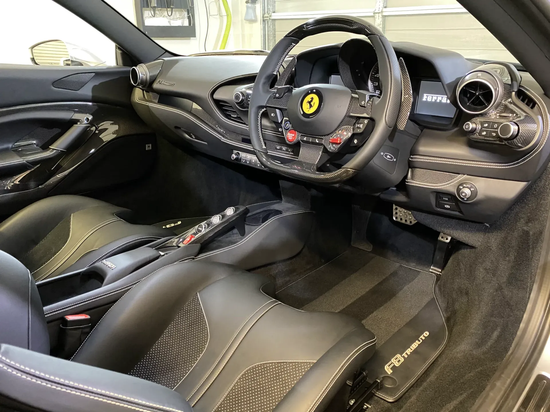 Interior view of a Ferrari sports car with black leather seats, dashboard, and steering wheel; carbon fiber accents.