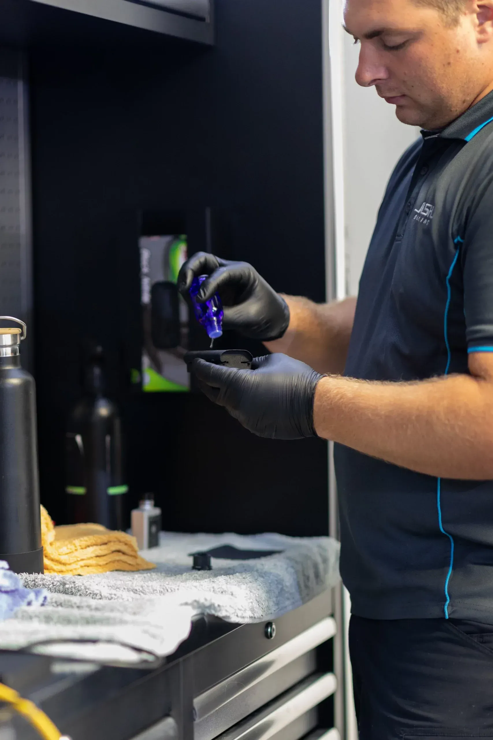 Man in black gloves, applying a liquid to a part, at a workbench in a workshop.