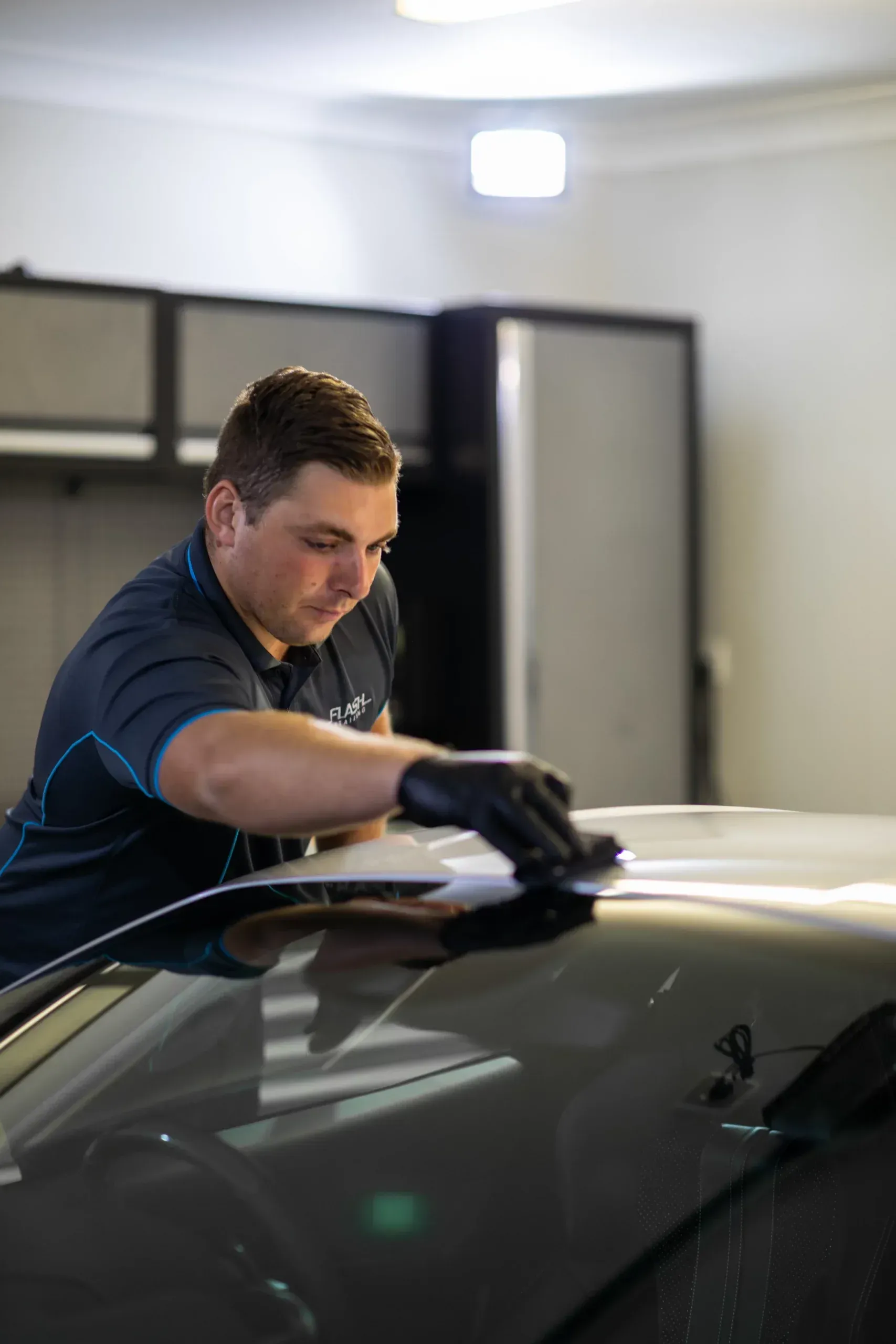 Man in black gloves, applying something to a car hood inside a garage.