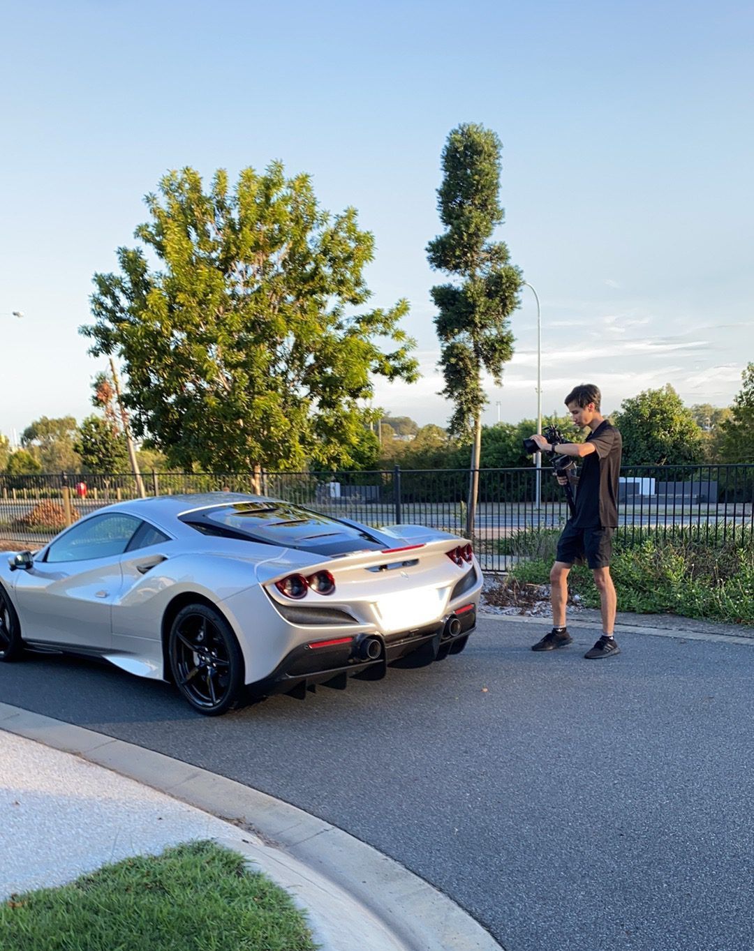 Silver Ferrari sports car parked on a road, a person taking a photo nearby.