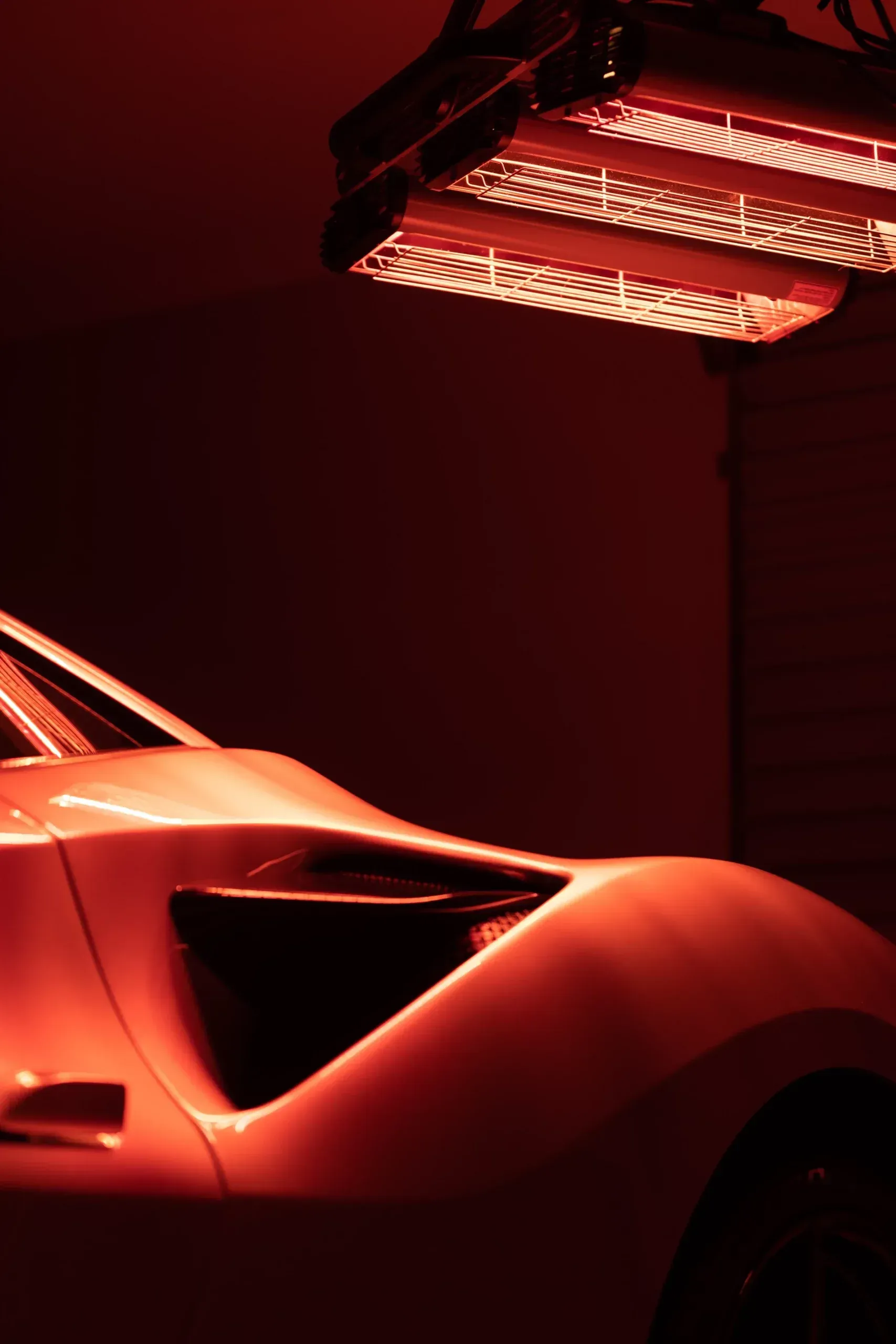 Red light illuminates a white sports car in a dark garage.
