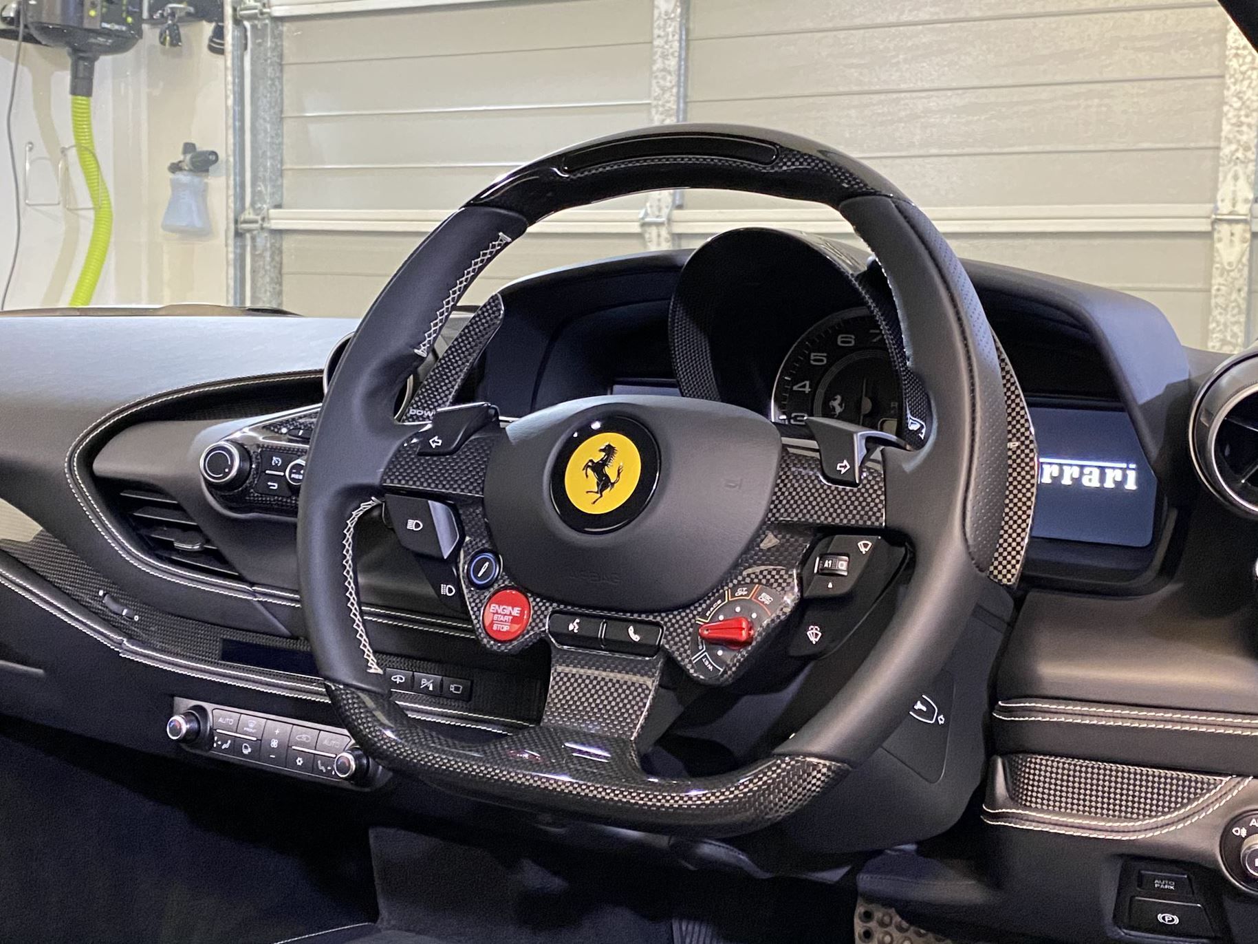Black Ferrari steering wheel with carbon fiber accents, red start button, and dashboard details.