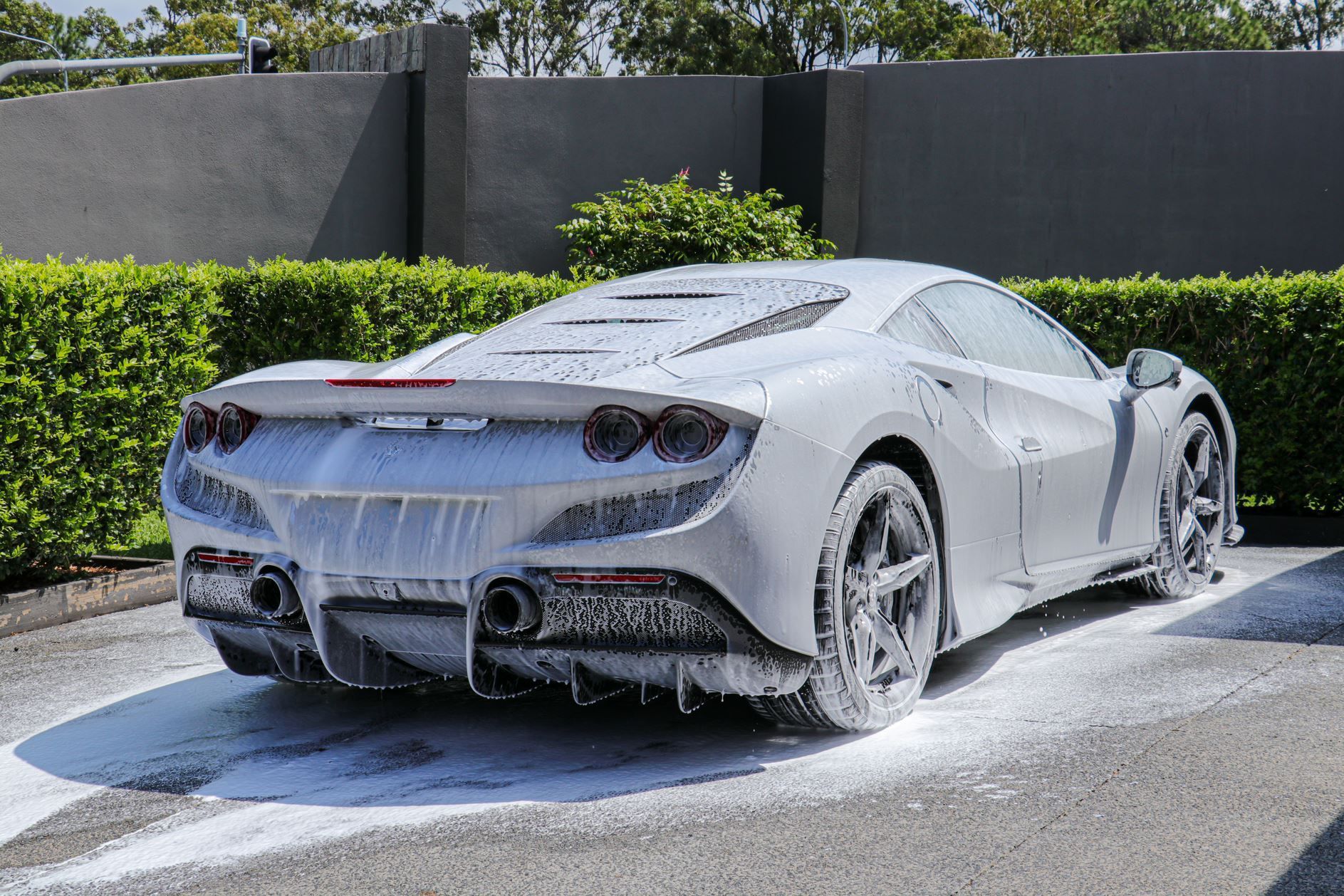 White sports car covered in soap suds, parked outside, being washed.