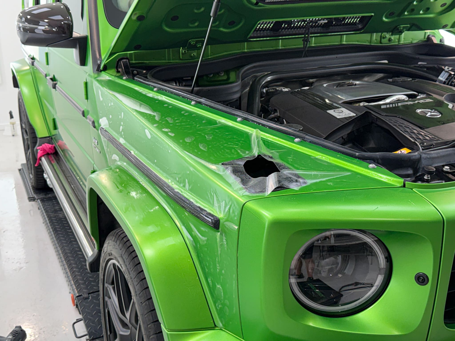 Bright green Mercedes-Benz G-Class SUV parked in front of a gray building with a closed garage door.