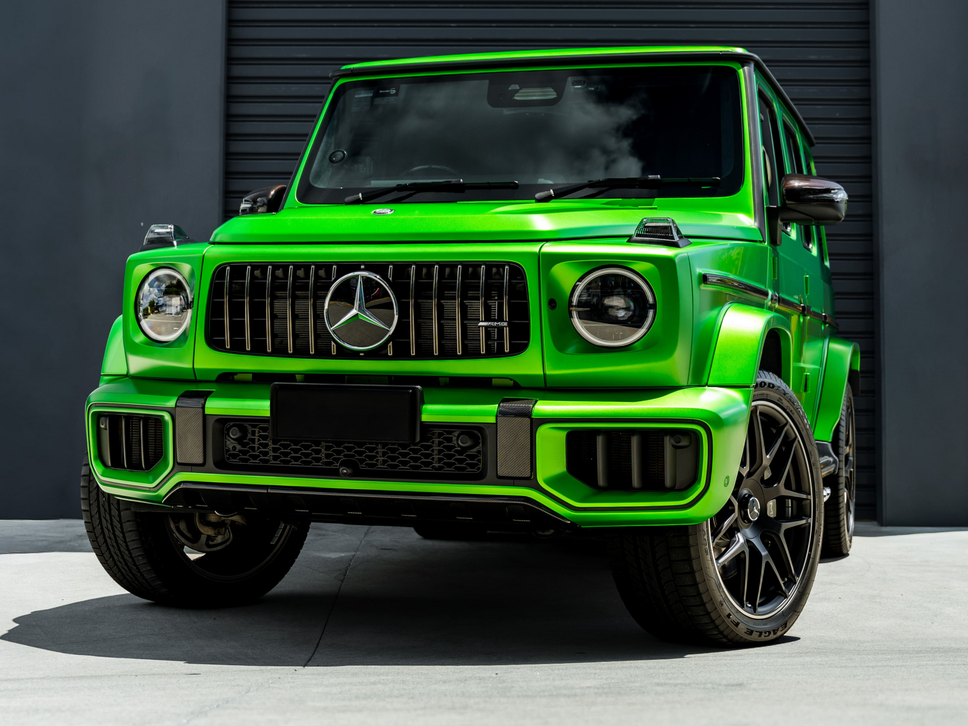 A bright lime-green Mercedes-AMG G-Wagon parked on a concrete surface against a dark gray shutter door.