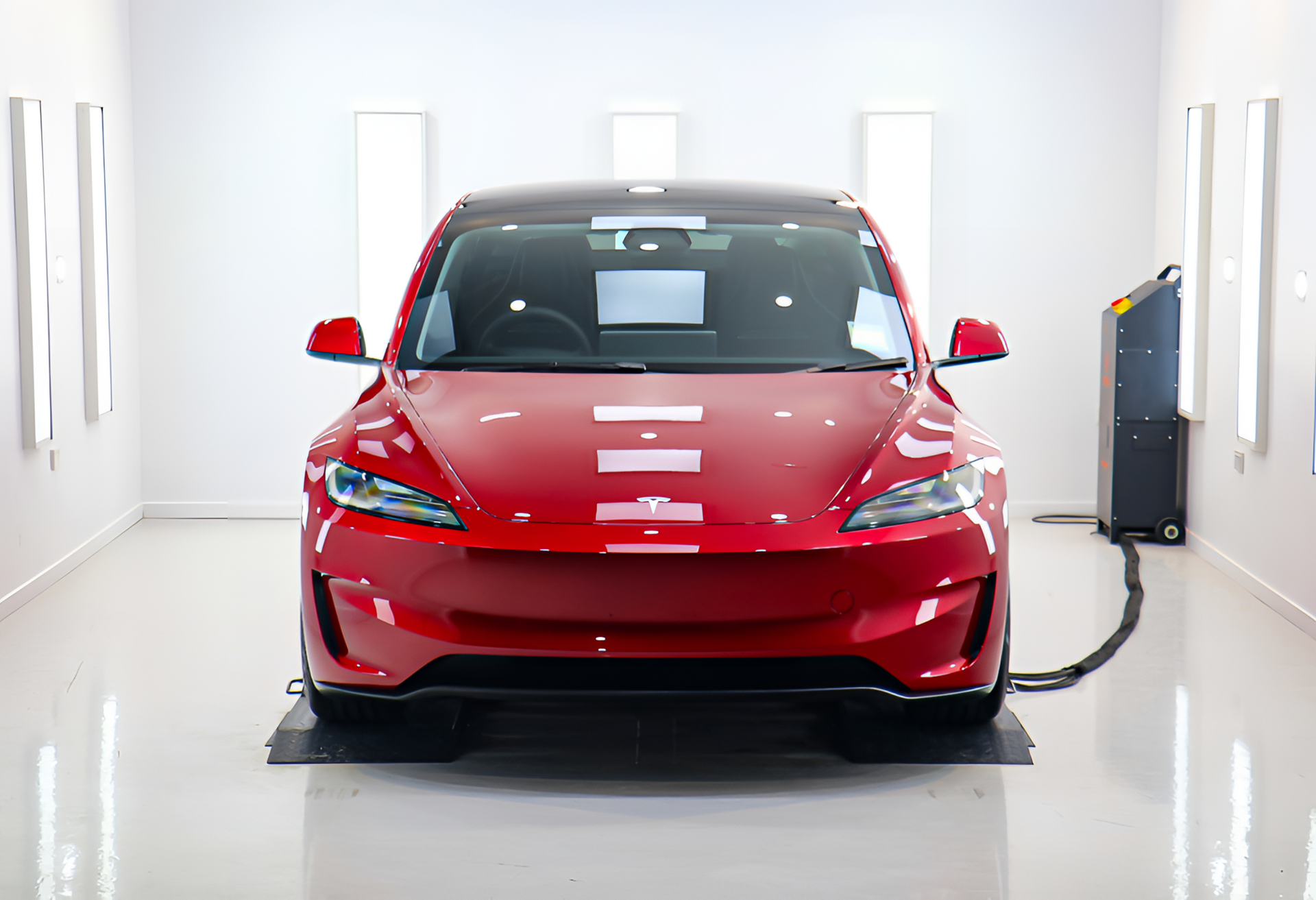 Red Tesla Model Y inside a white, brightly lit workshop.