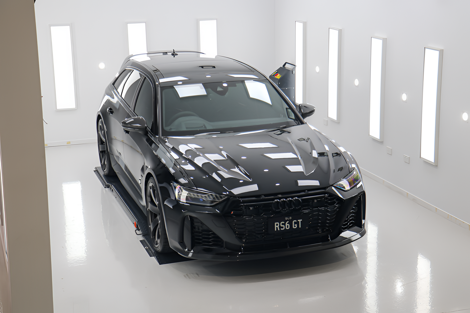 A black Audi RS6 station wagon parked in a bright, white studio with vertical light panels on the walls.