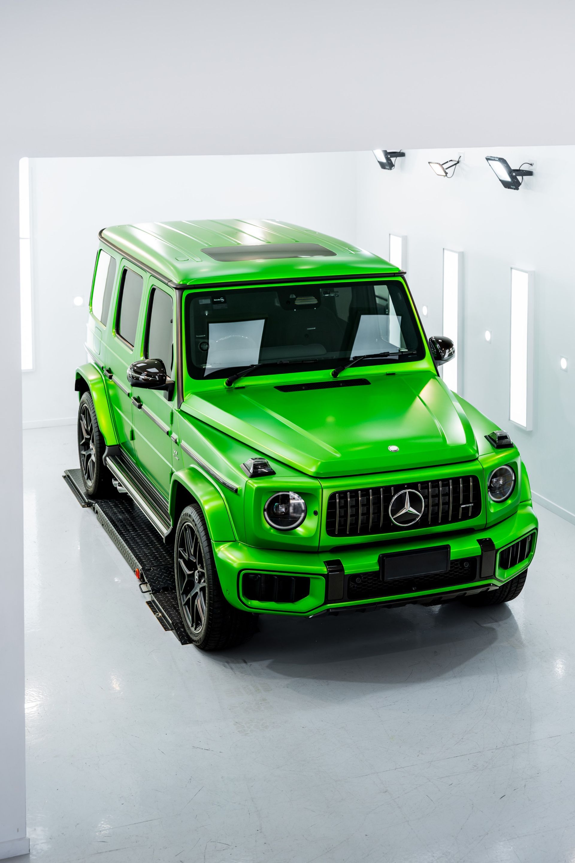 Bright green Mercedes-Benz G-Class SUV in a white-walled studio, front view.