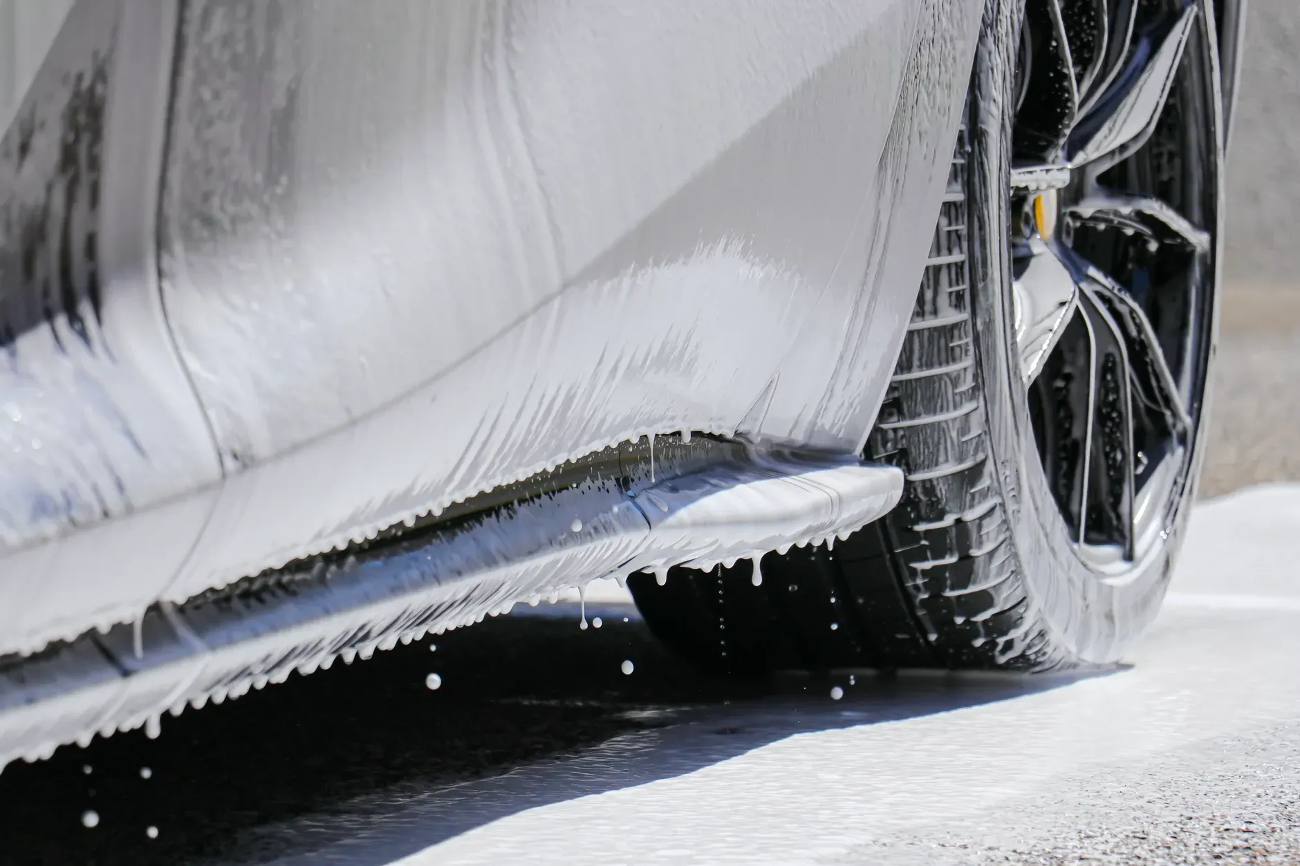 Car being washed with foamy soap. Black tire and side skirt visible.