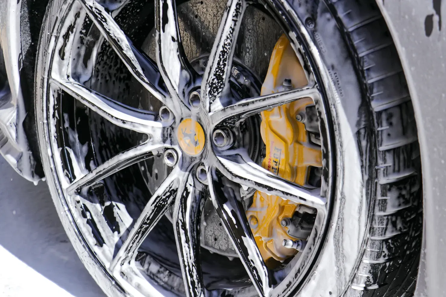 A gray sports car covered in white foam suds, being washed.