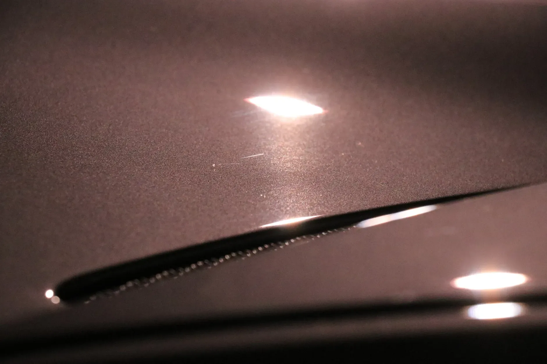 Close-up of a dark metallic surface with a long, thin, recessed area reflecting light.