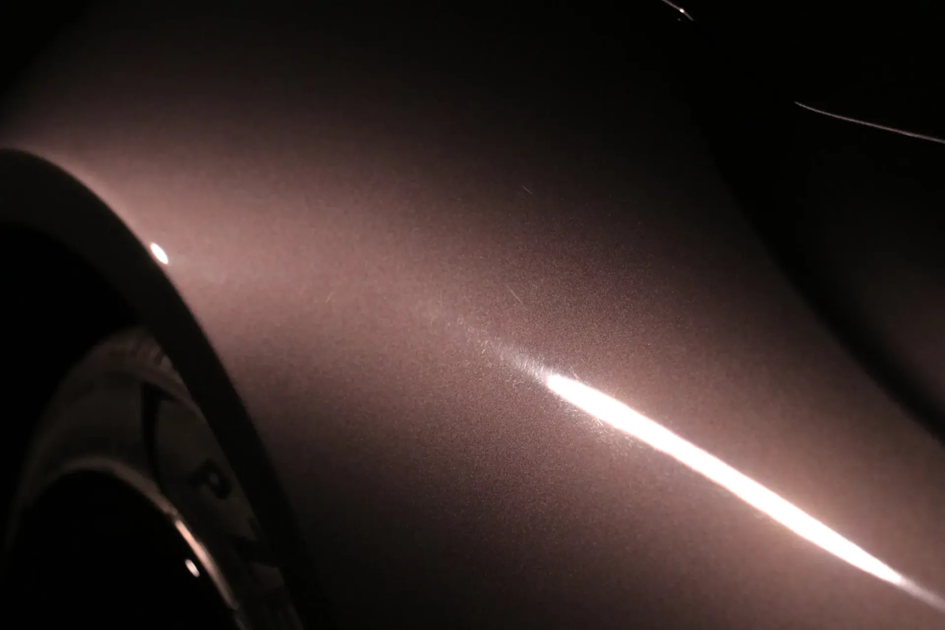 Close-up of a car's metallic, rose-colored body panel, with a reflection of light.