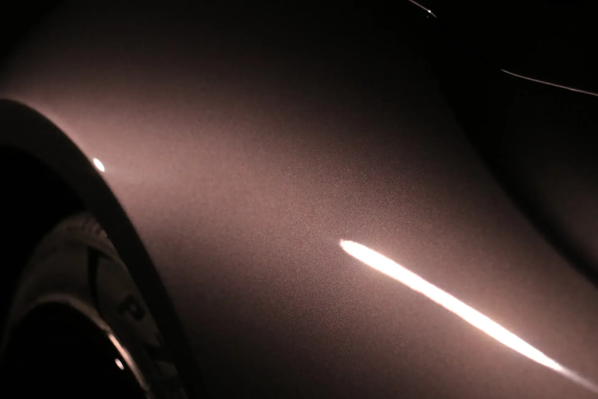 Close-up of a car's metallic, rose-toned fender with light reflections, slightly out of focus.