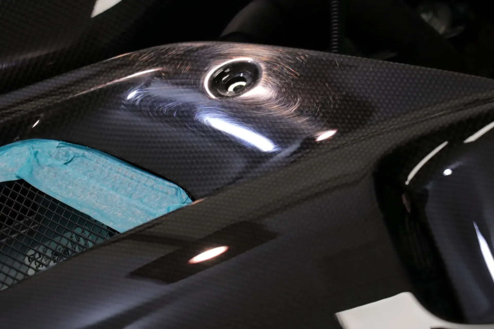 Black carbon fiber motorcycle bodywork with a visible fastener and blue foam padding.