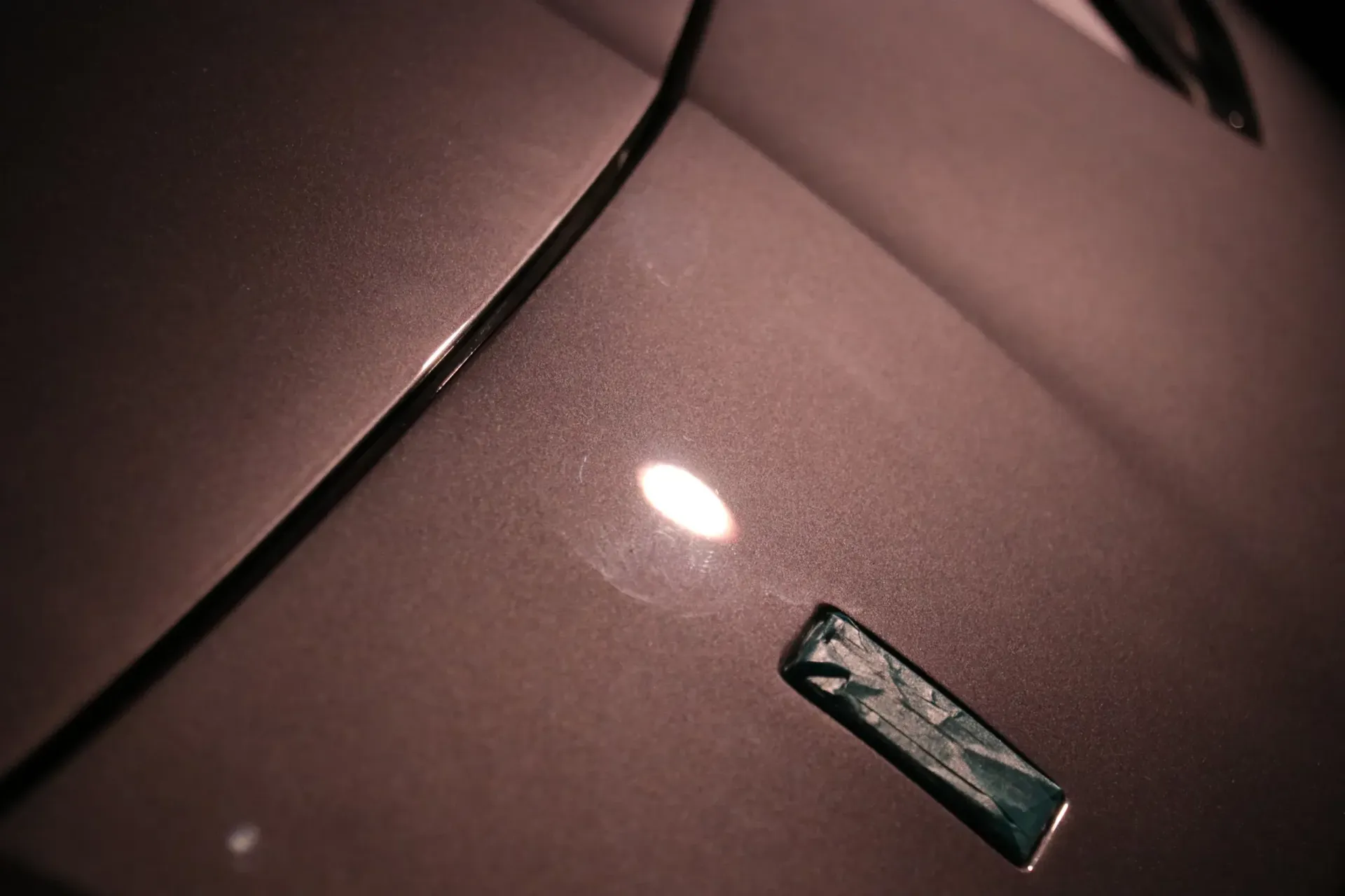 Close-up of a mauve-colored car hood with a shiny reflection and dark trim.