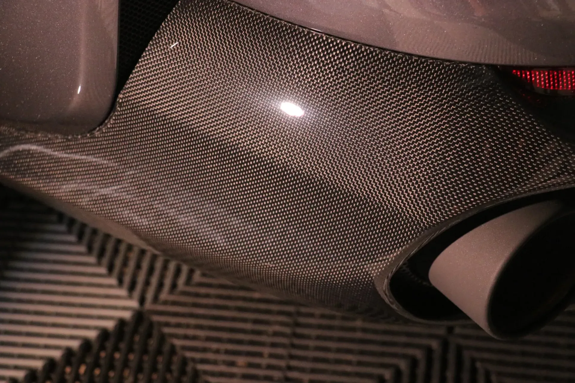 Close-up of a car's carbon fiber rear underbody with dual exhaust pipes.