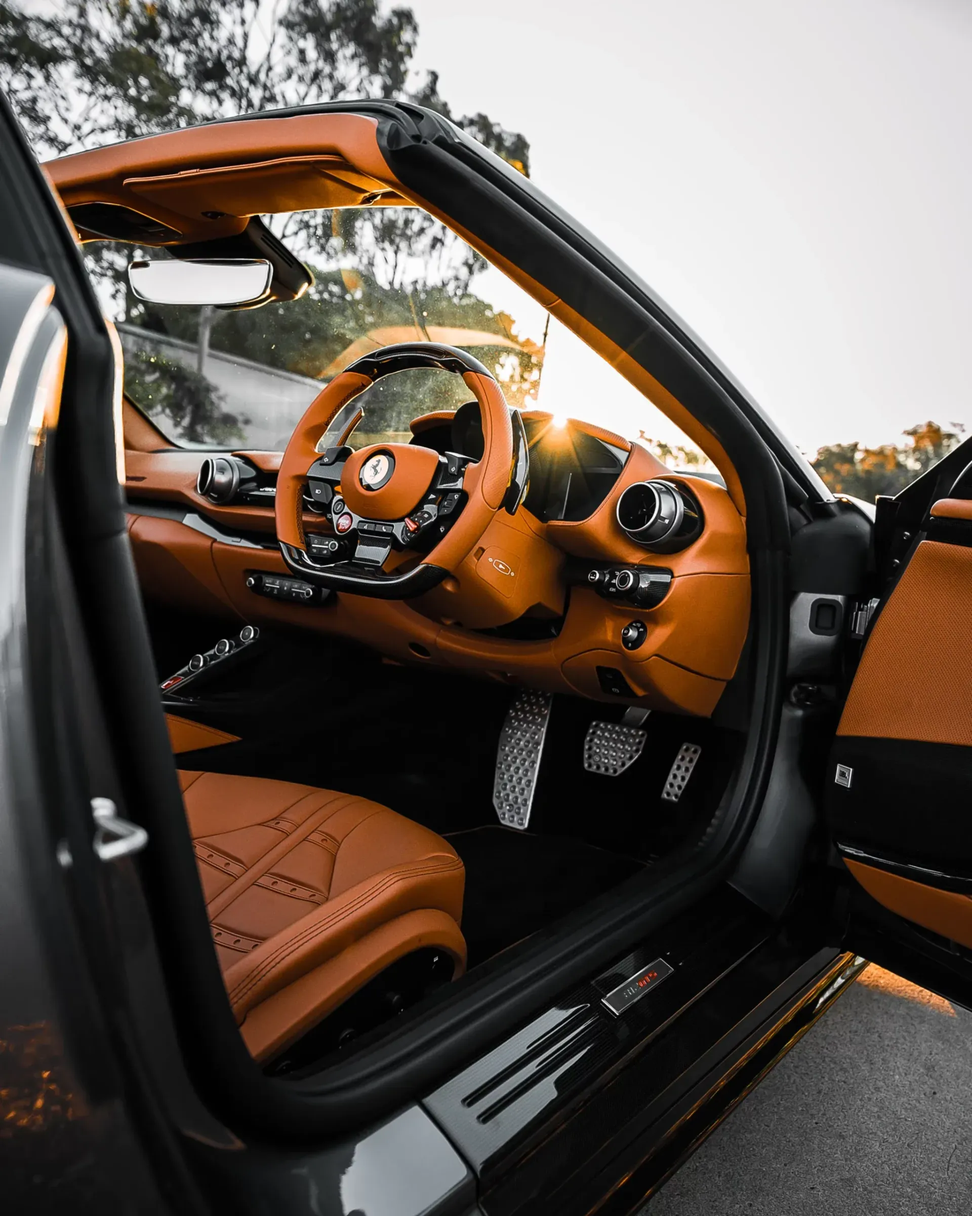 Luxurious car interior with tan leather accents, steering wheel, and open door.