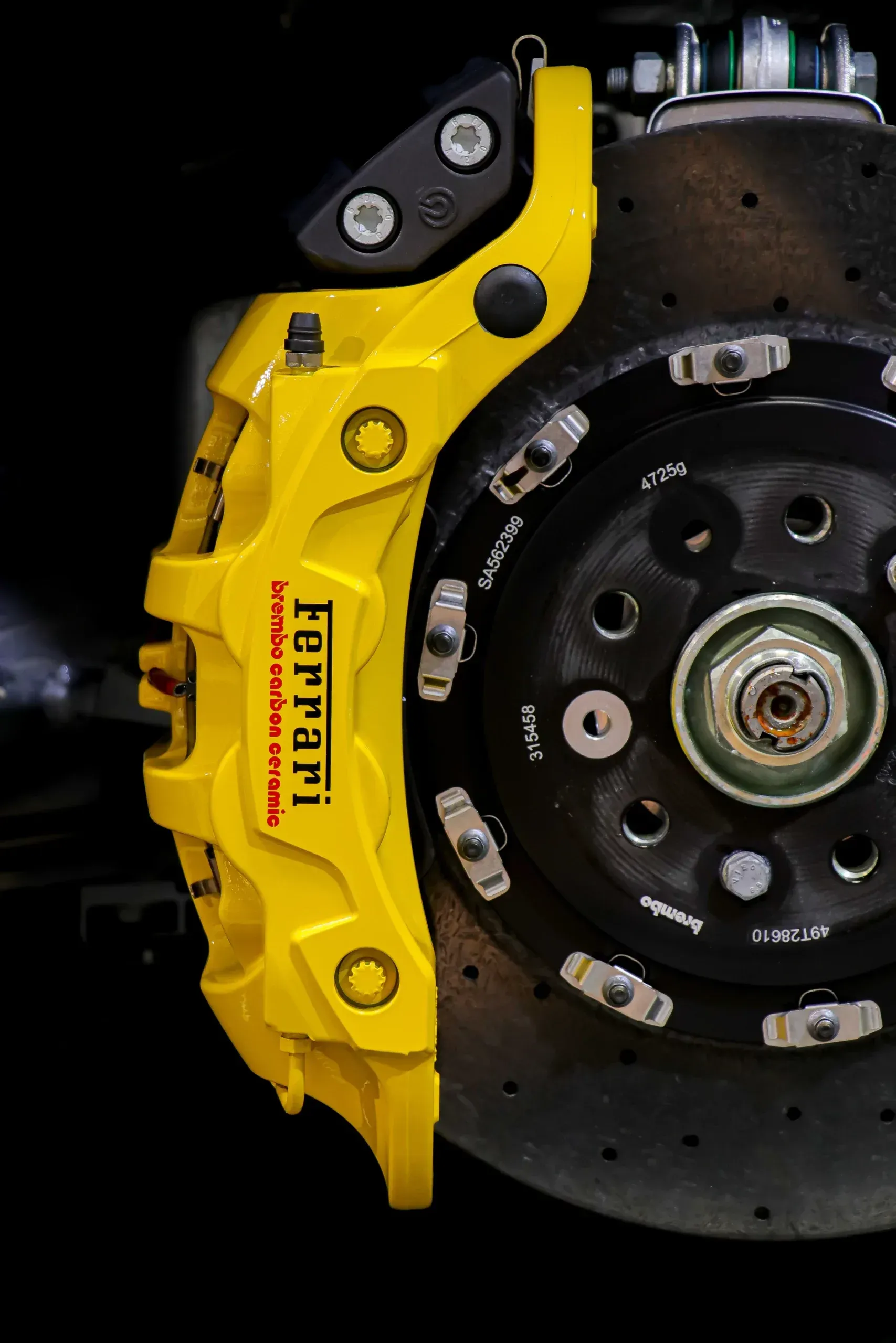 Yellow Ferrari brake caliper on a slotted rotor; black background.