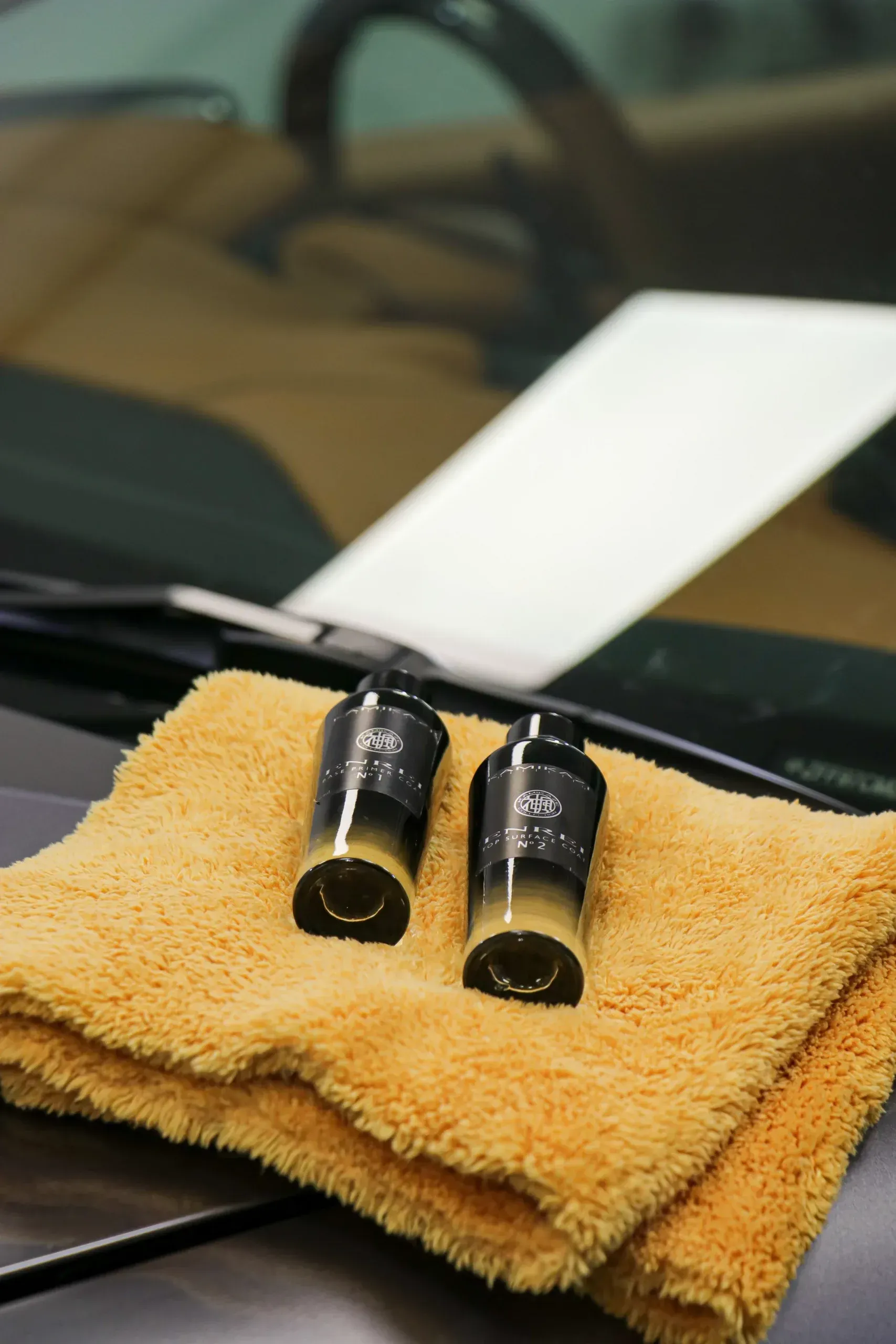 Two black and gold objects on an orange cloth rest on a car's hood, windshield and interior in background.