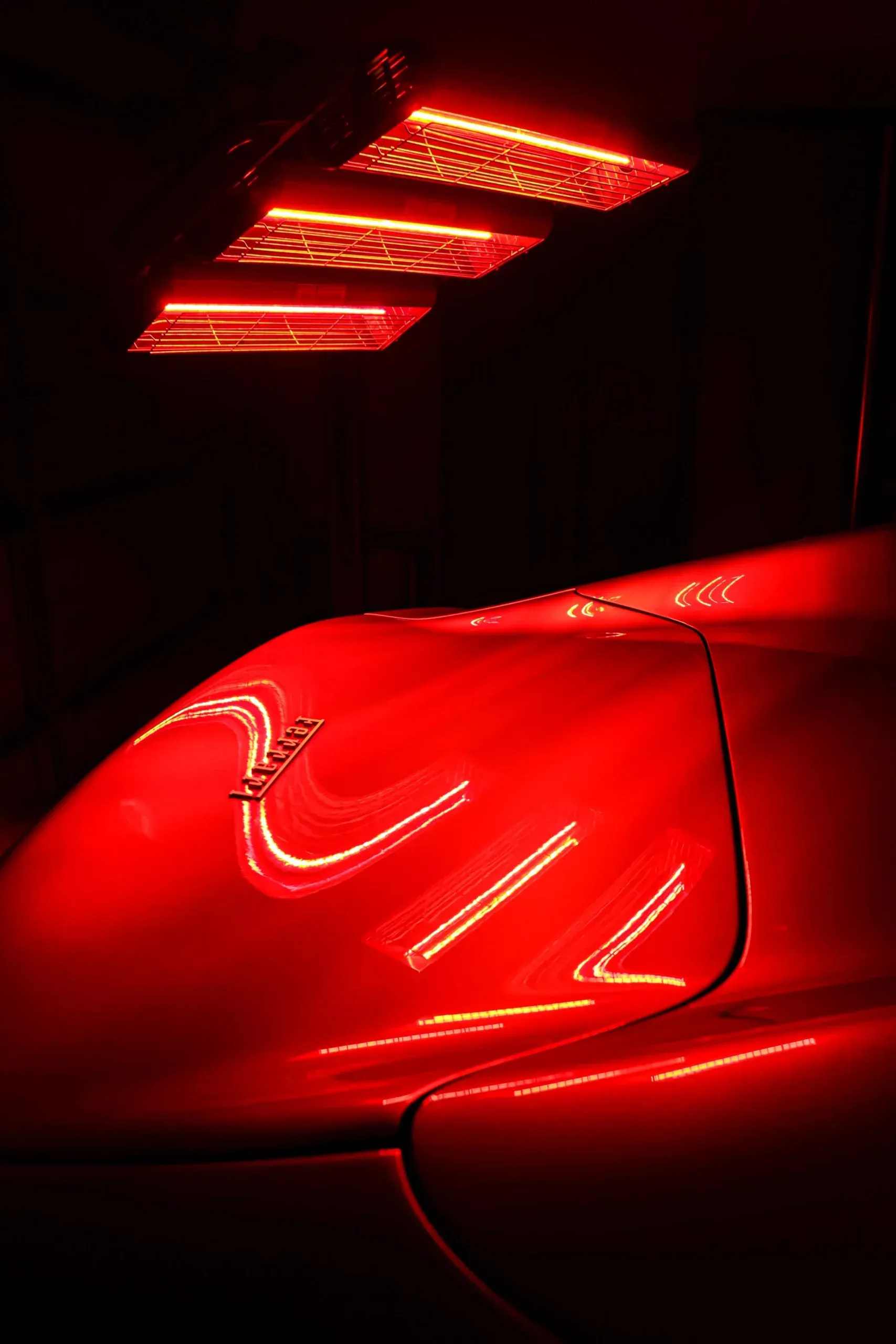 Red lights illuminating a red sports car in a darkened garage.