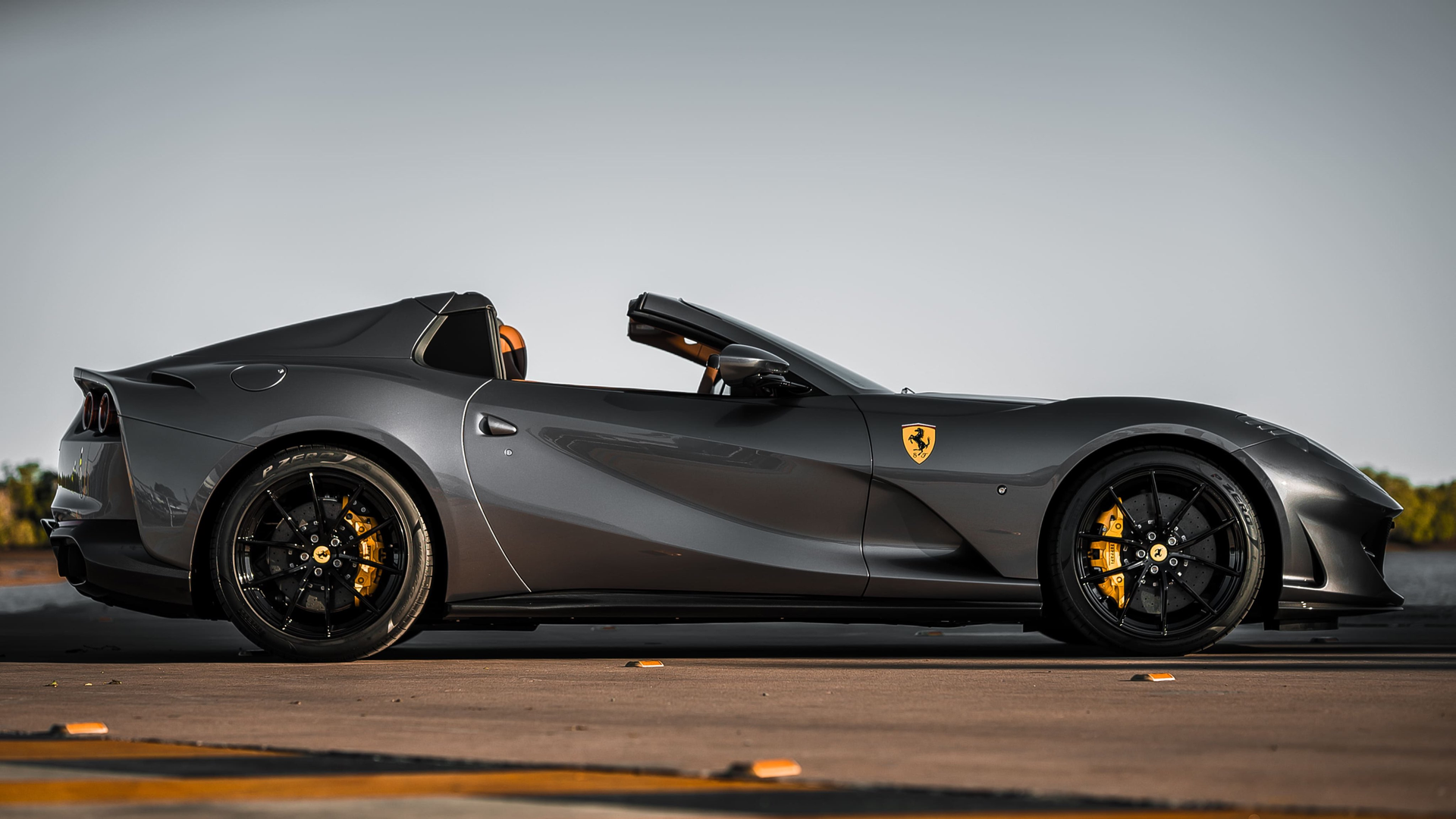 Dark gray Ferrari convertible with black wheels, golden brake calipers, and a sunny outdoor setting.