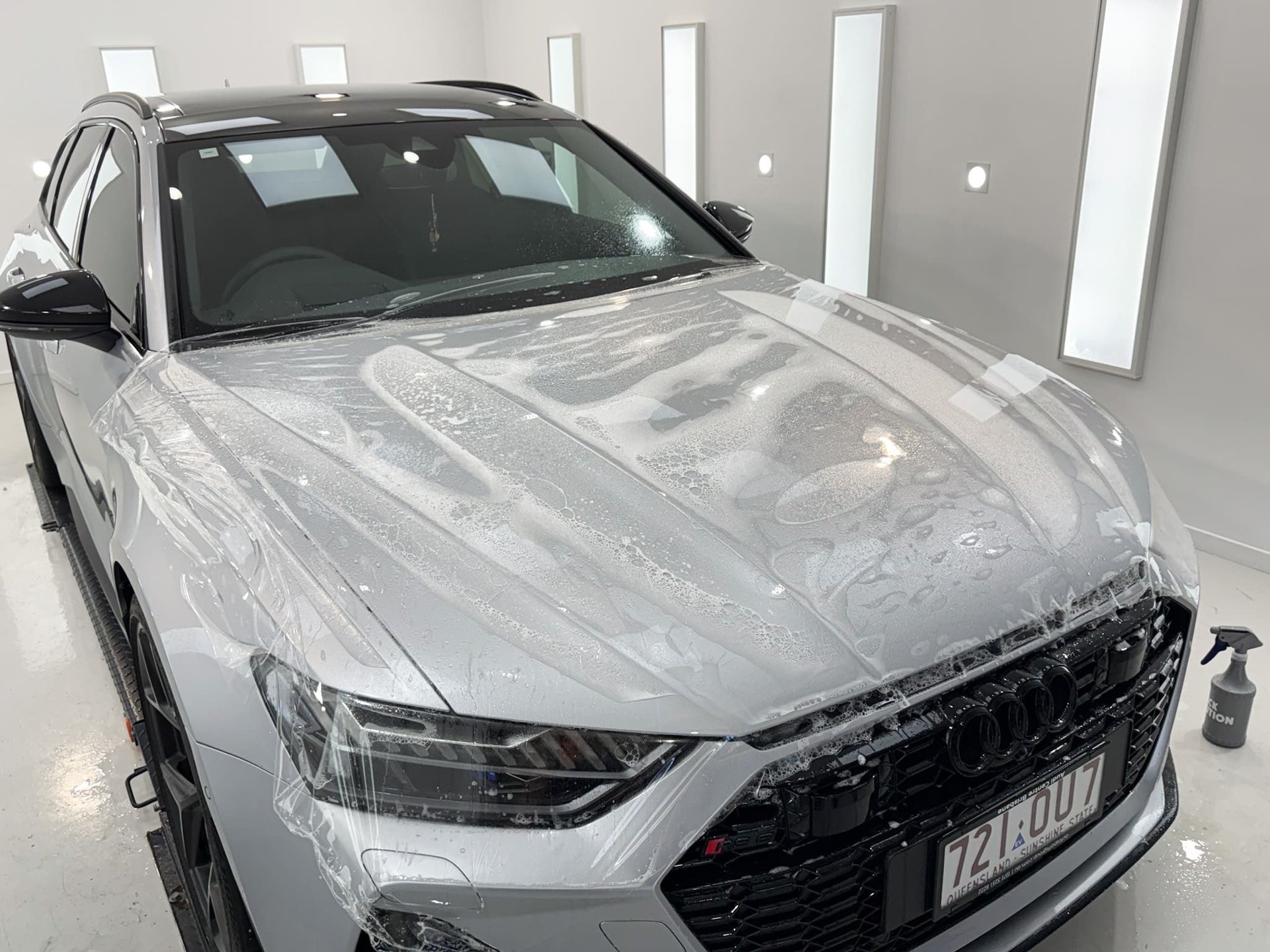 Man applying film to a black car surface with a squeegee, in a bright workshop.