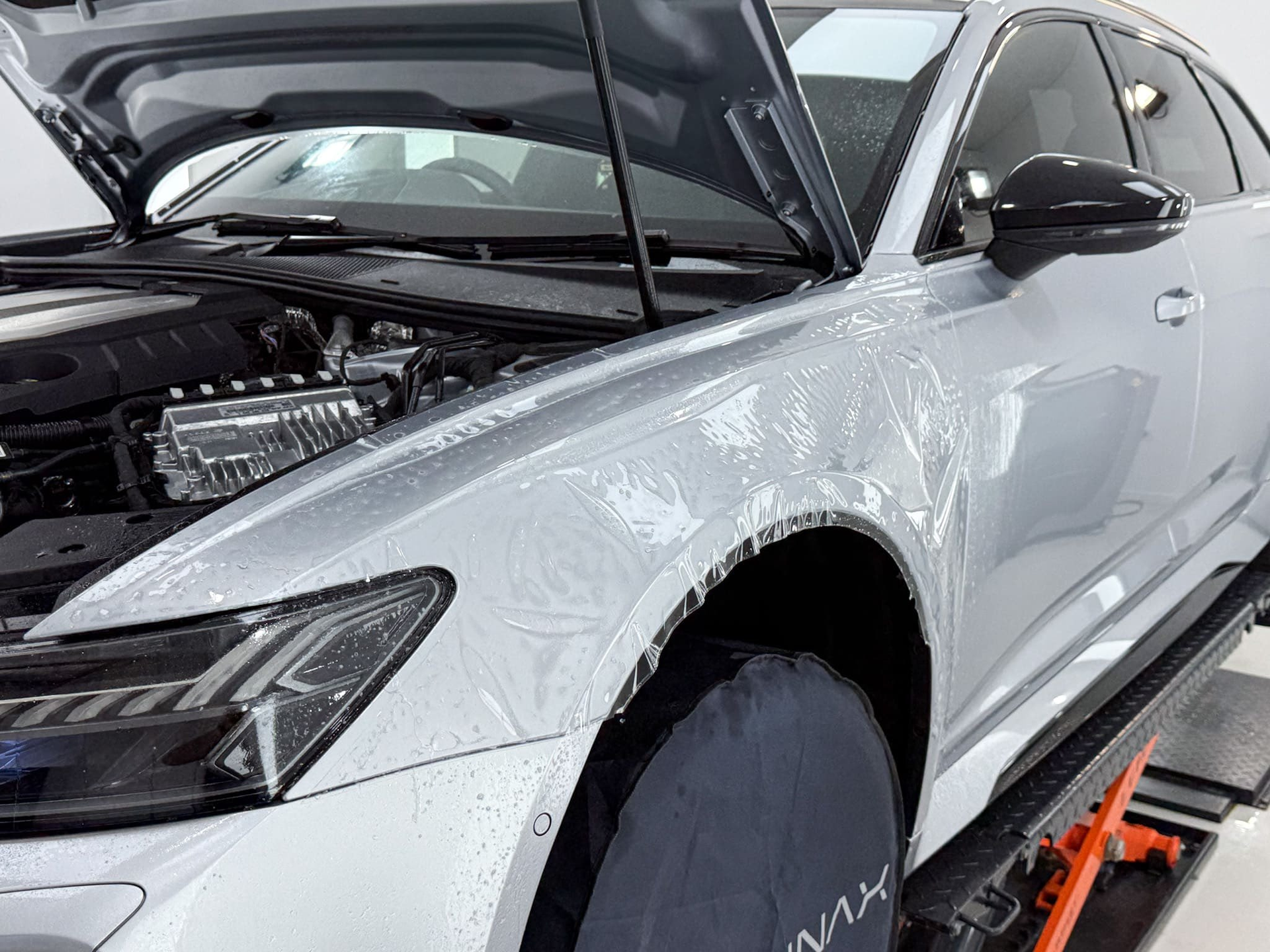 Man applying film to a black car surface with a squeegee, in a bright workshop.
