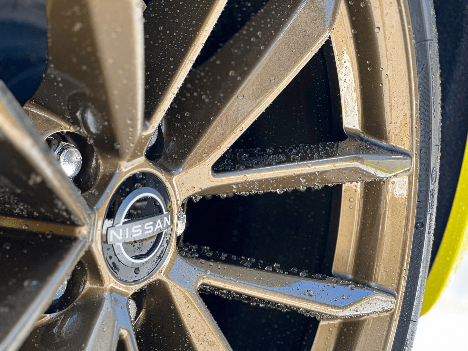 Gold-colored Nissan car wheel with water droplets, logo visible.