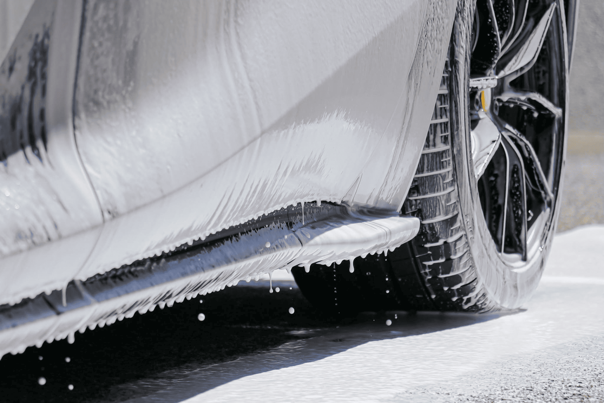 Car being washed with white foam, focus on side skirt and tire.