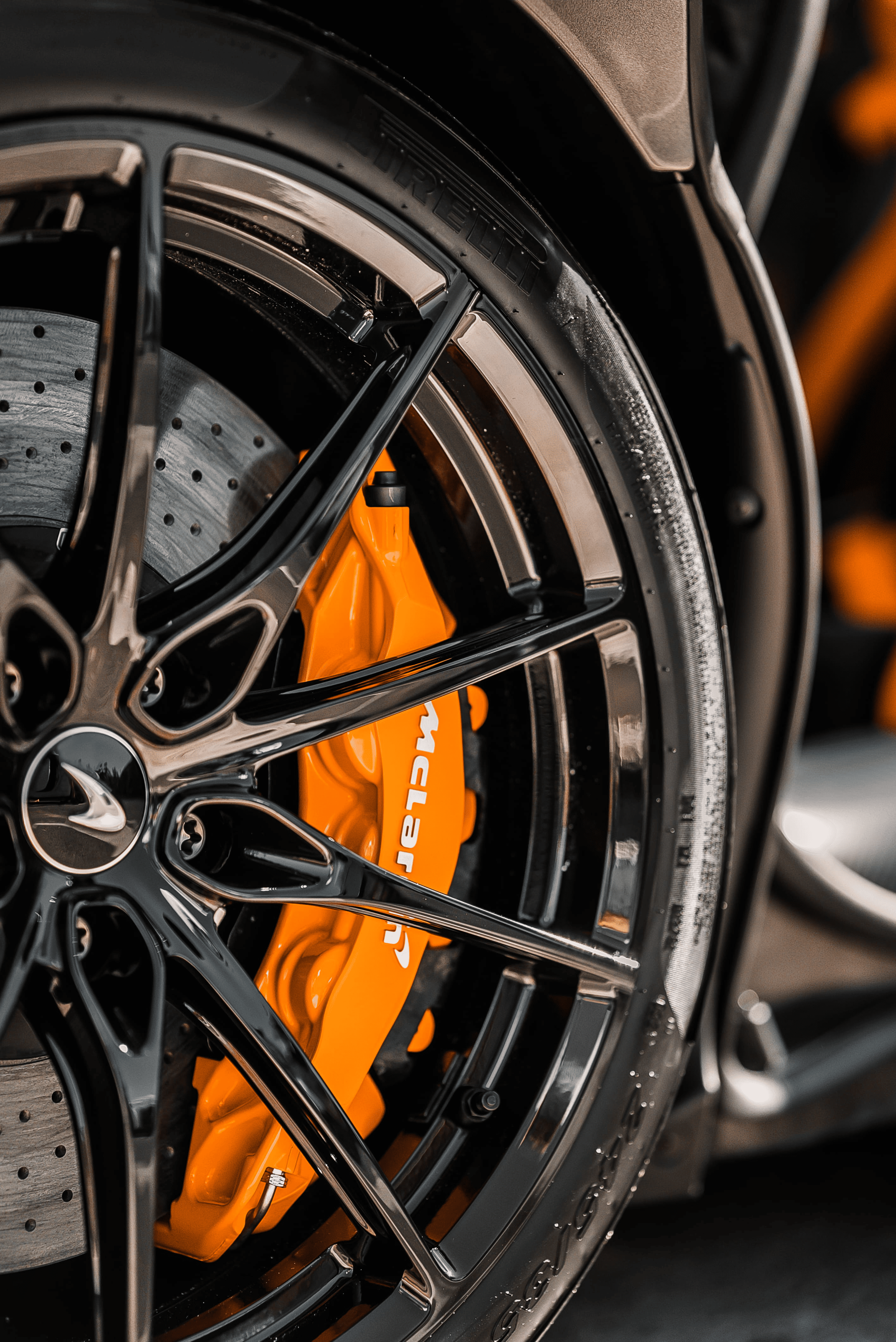 Close-up of a glossy black car wheel with bright orange McLaren-branded brake calipers.