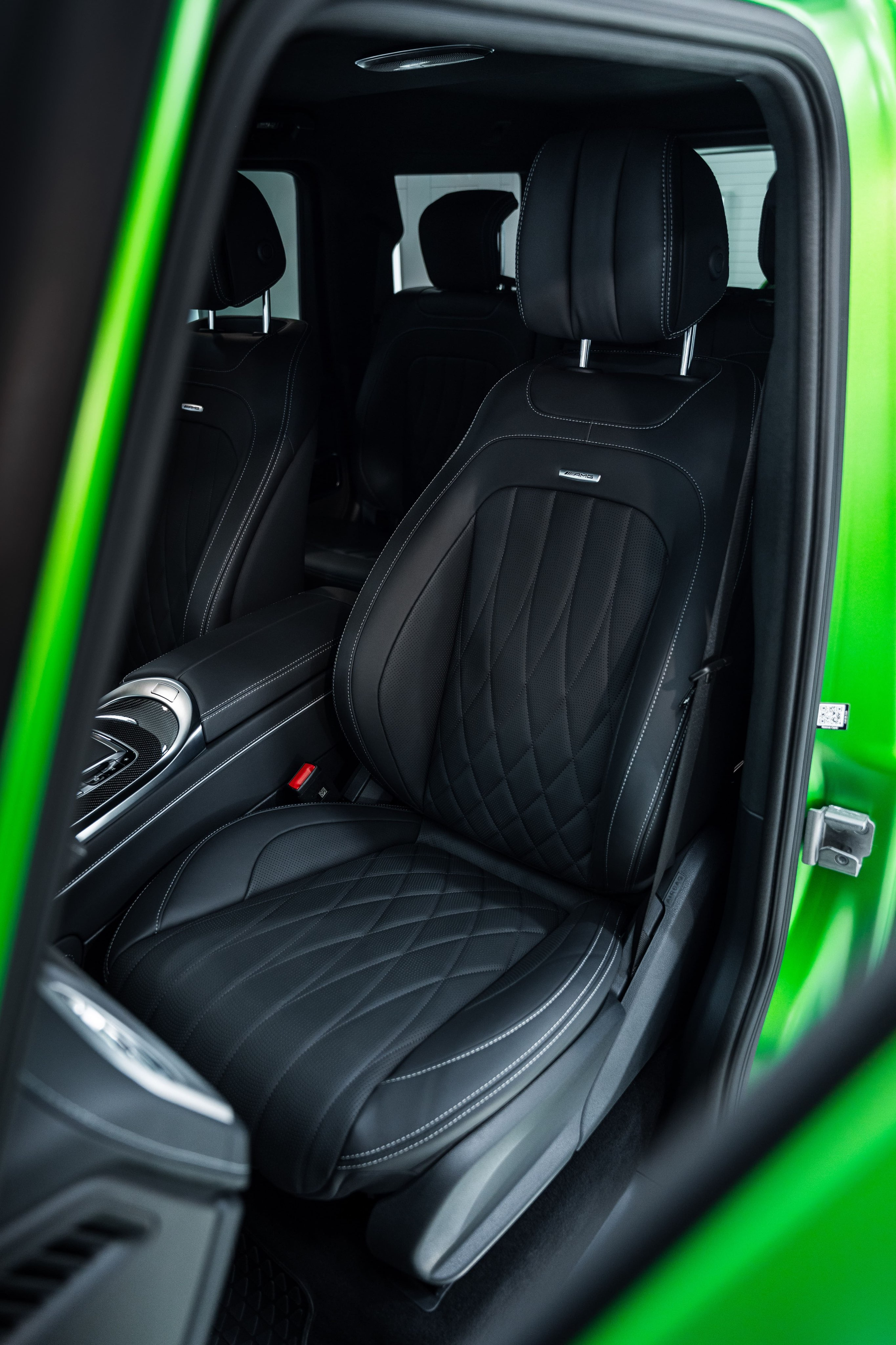 Black leather car seat with diamond stitching, inside a green vehicle.
