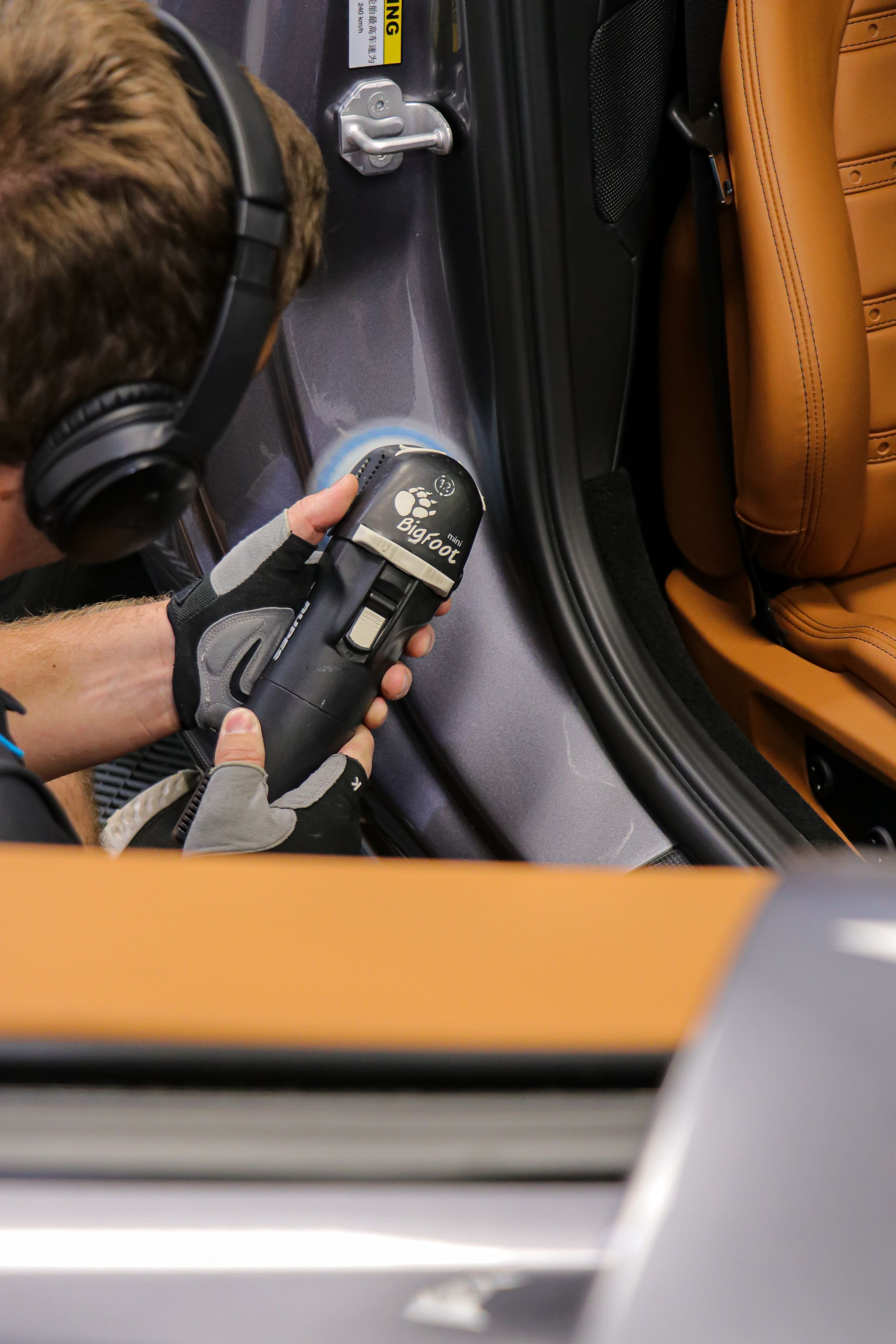 Person using a buffer to polish the side of a silver car. Glove visible on hand.