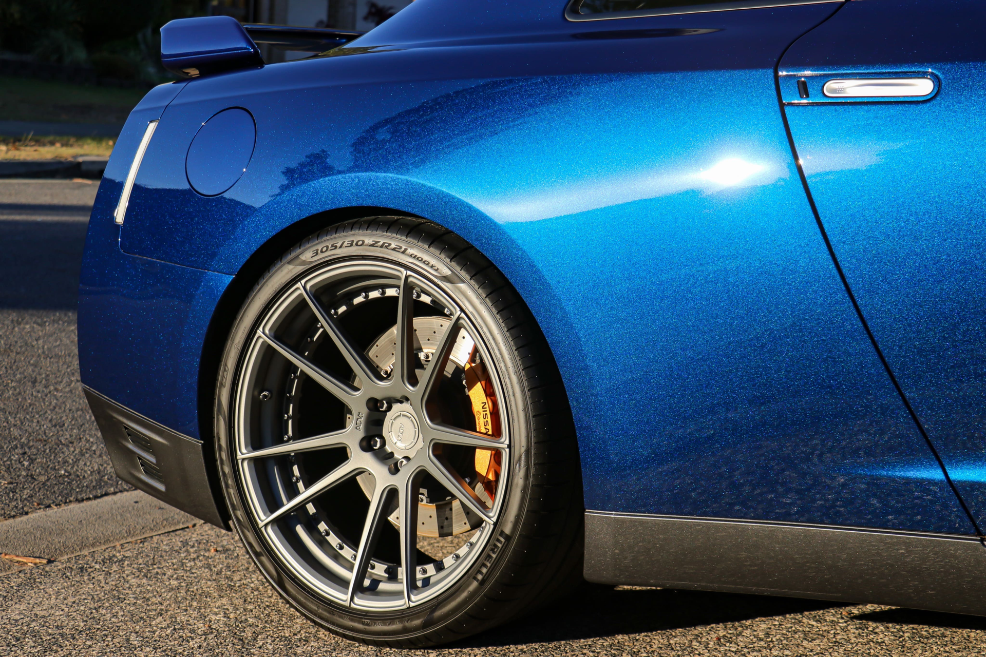 A close-up of the rear quarter panel and custom grey multi-spoke wheel of a metallic blue sports car.