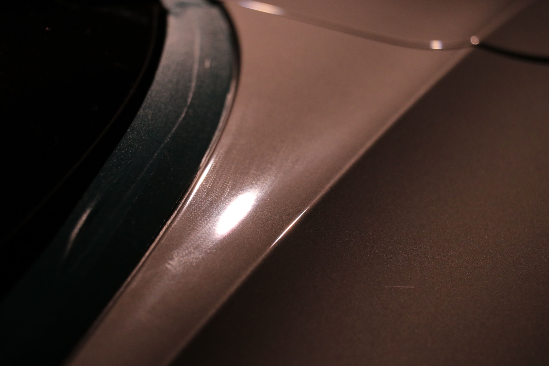 A close-up of a smooth, metallic-painted vehicle body panel with a dark window trim and a bright reflection.