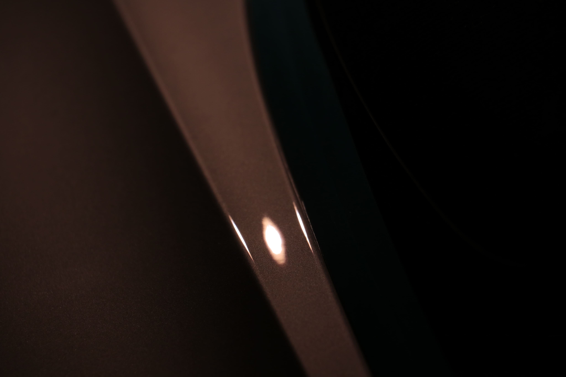 A close-up, abstract view of a smooth, curved light-colored surface with a single bright highlight against a dark background.