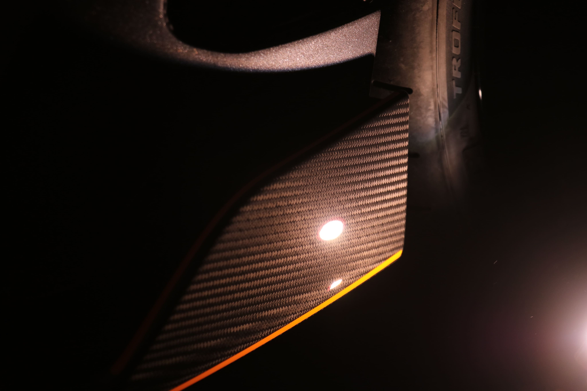 Close-up of a carbon fiber surface with a yellow edge, angled against a dark background with a bright light reflection.