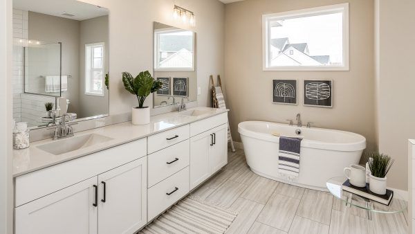 Spacious bathroom with white cabinets, tub, and light-colored flooring. Window provides natural light.