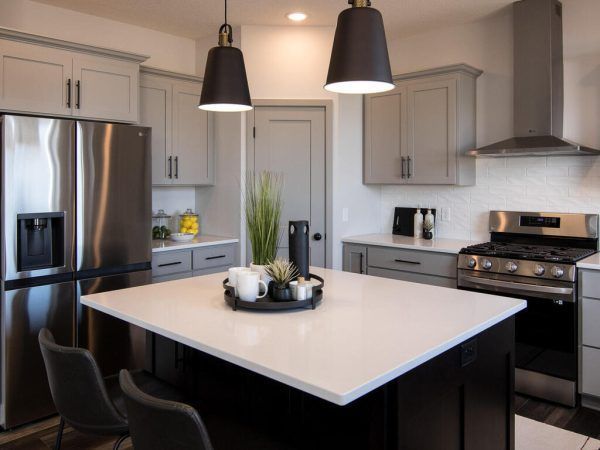 Modern kitchen with gray cabinets, black island, stainless steel appliances, and pendant lights.