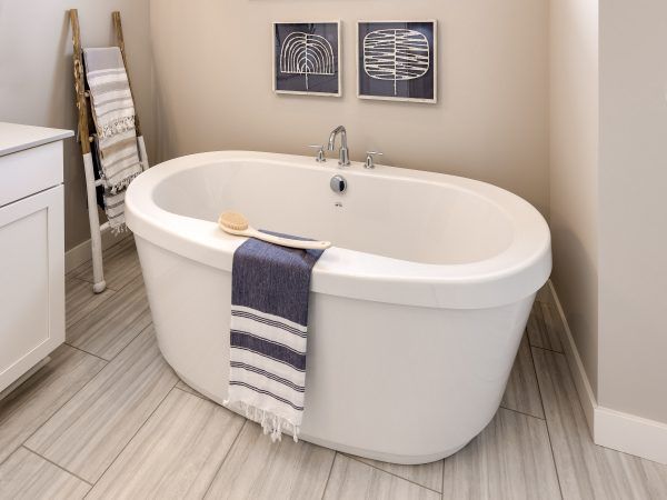 Oval white bathtub in a neutral-toned bathroom with a towel and artwork above.