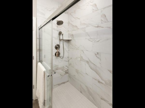 White tiled shower with glass sliding door, chrome fixtures, and towel.