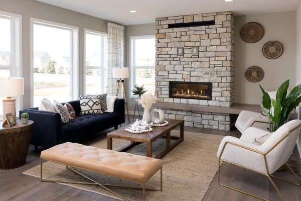 Living room with stone fireplace, dark blue sofa, wood coffee table, light chairs, and large windows.