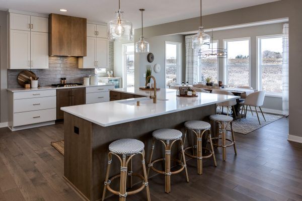 Modern kitchen with island, white cabinets, wooden accents, and dining area with large windows.