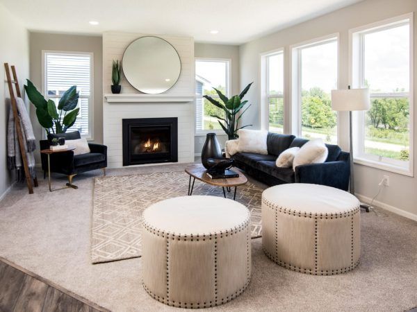 Living room with fireplace, black sofa, and two ottoman seats, neutral colors, large windows.