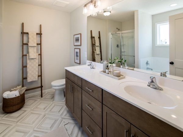 Bathroom with double vanity, wood cabinets, ladder towel rack, and patterned floor tiles.