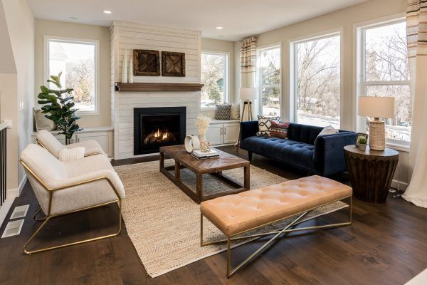 Living room with fireplace, white and gold seating, navy sofa, and large windows overlooking a winter scene.