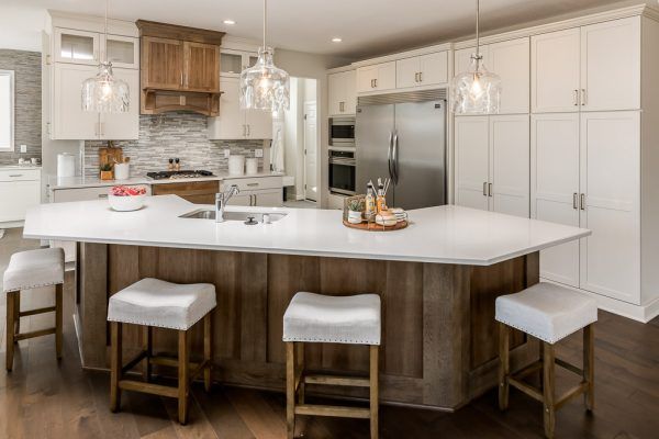 Kitchen with large island, white cabinets, and wood accents. Three bar stools sit at the island.