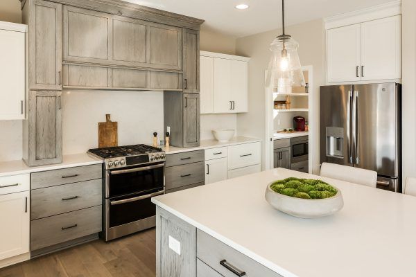 Modern kitchen with gray and white cabinets, stainless steel appliances, and a white island.