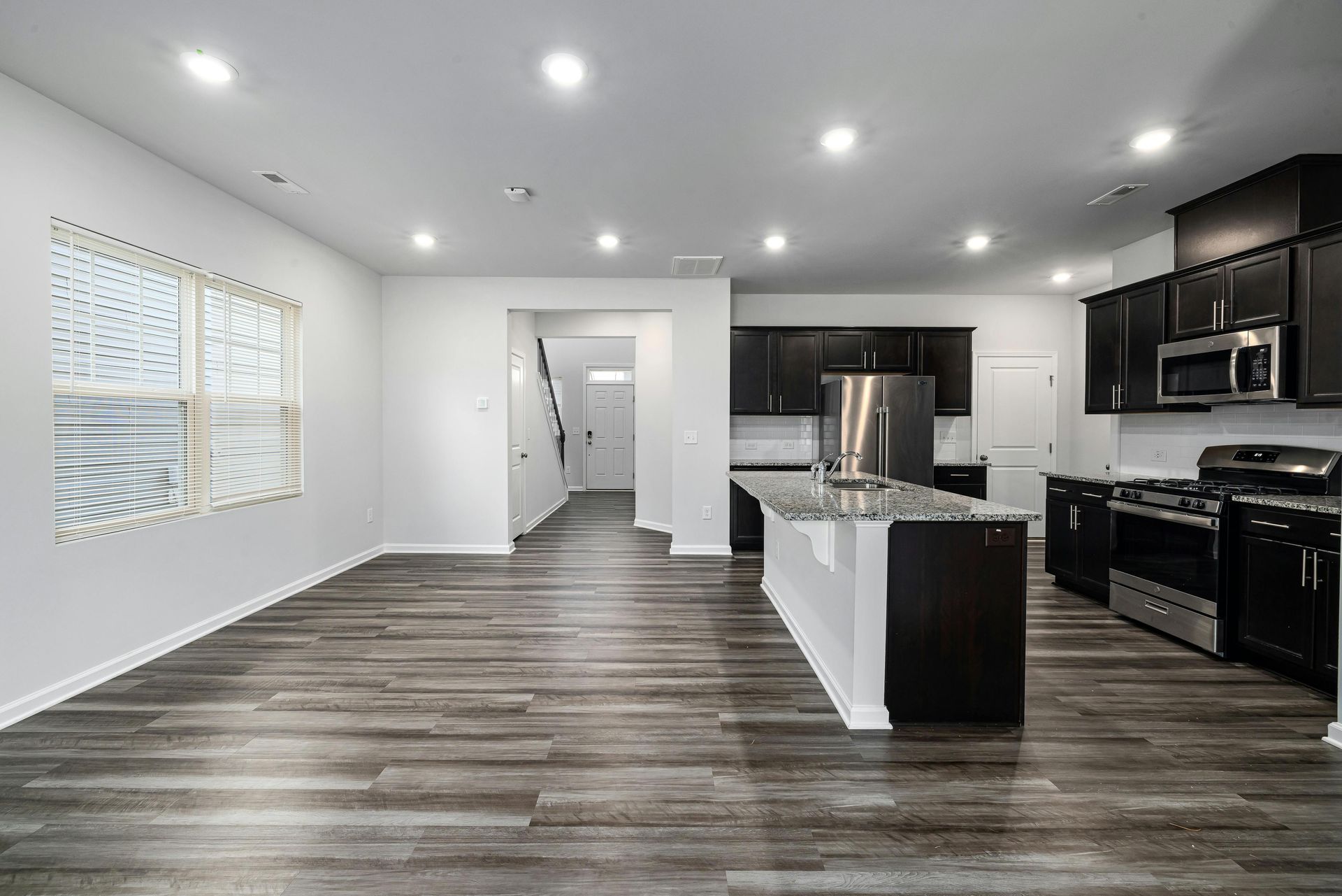 Open-concept kitchen and living area with dark cabinets, granite island, and gray wood flooring.