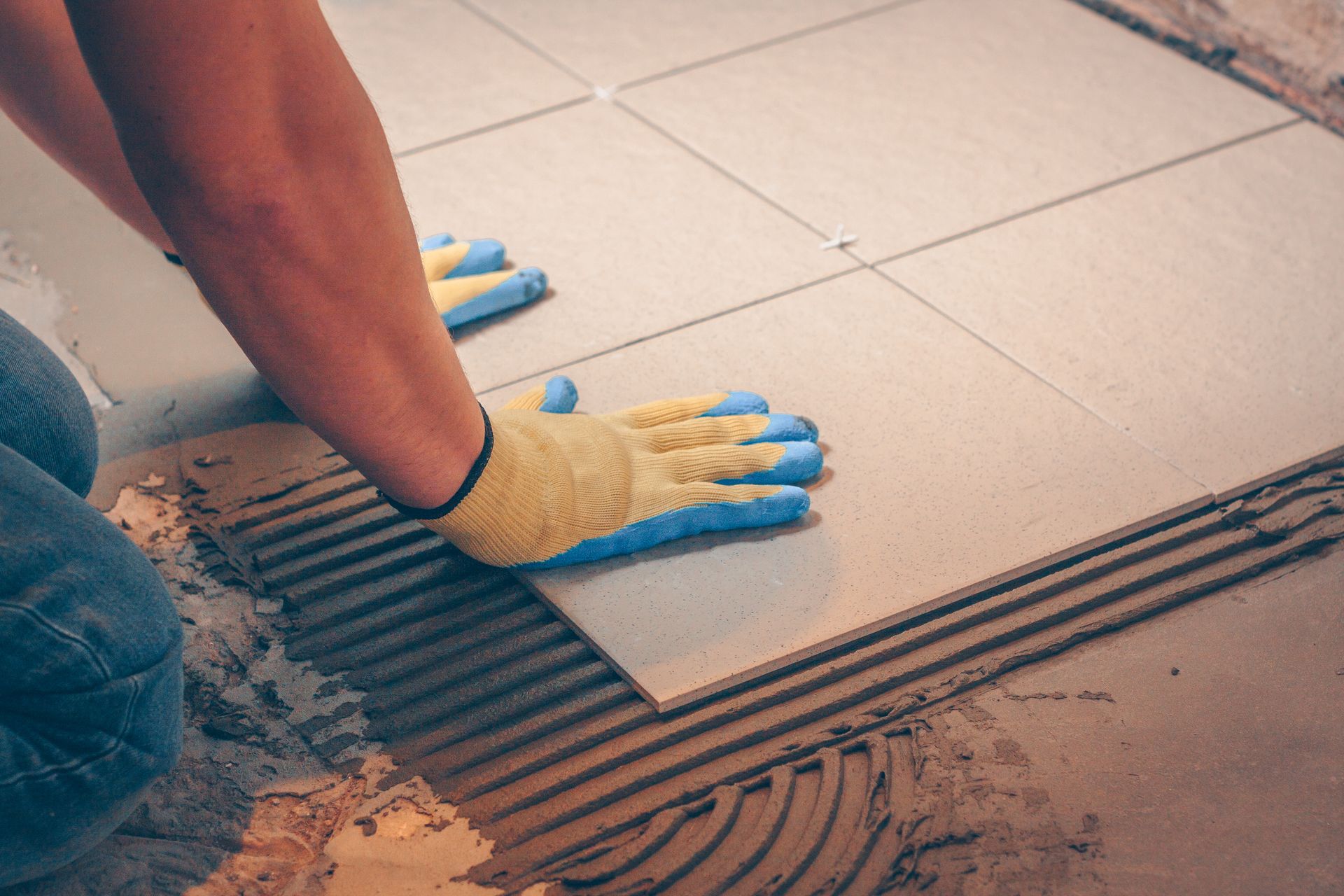 Person wearing gloves laying a tile on a floor.